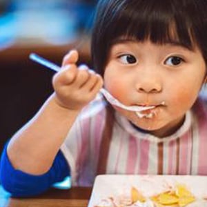 Little Asian girl eating with a fork