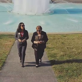 Two women walking on a pathway in front of a water fountain