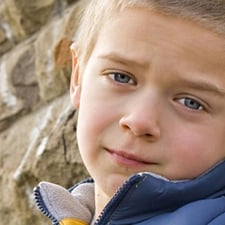 Photo of blond hair boy standing against a wall