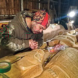 A man working on a wood-carving of a totem pole