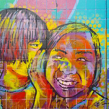 A colorful painted wall mural depicting two children sharing a private conversation
