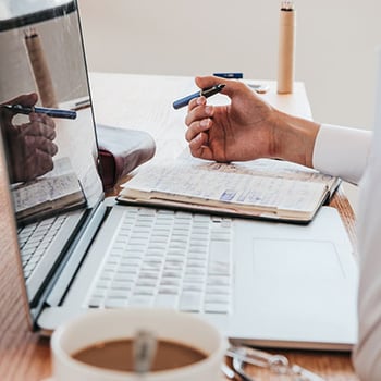 Close up photo of a man working at his desk in front of a laptop with coffee