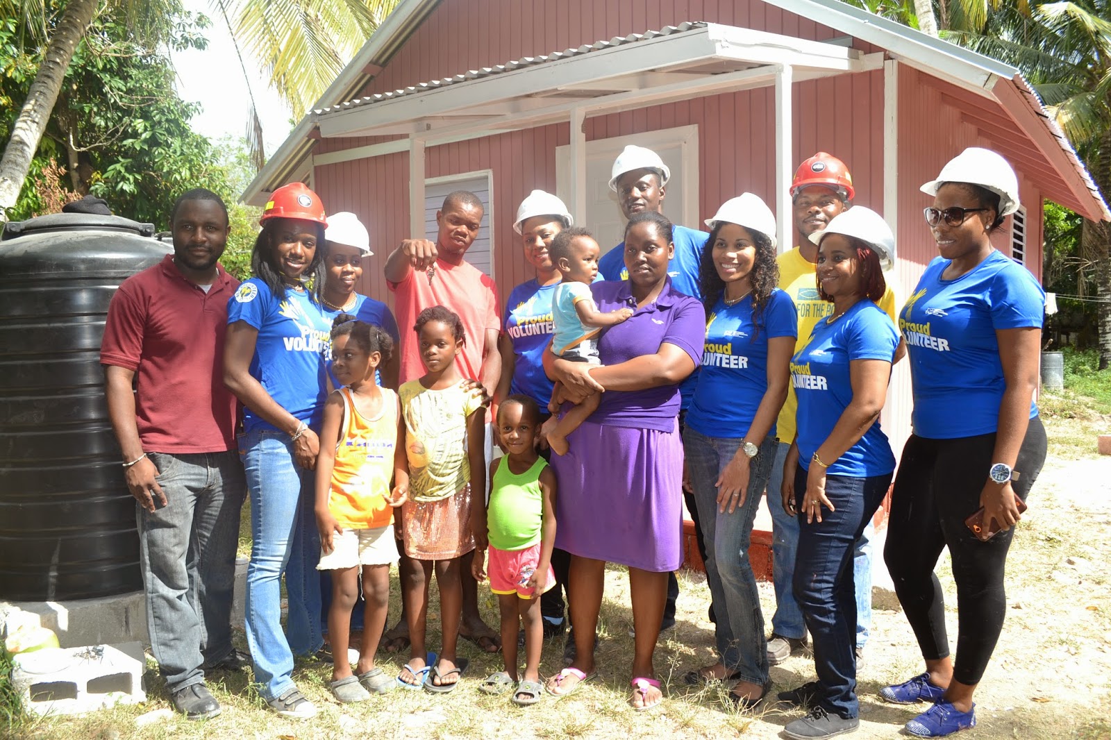 Volunteers from the National Commercial Bank Foundation and Food For The Poor Jamaica, standing before the new house that was constructed for a family in need.