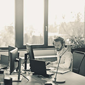 A man with headphones on working on a desk top computer by the window