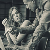 A man and a woman discuss work at a desk in front of their computers