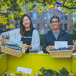 A man and a woman,smiling, each holding a basket of vegetables while selling at a vegetable stand outside